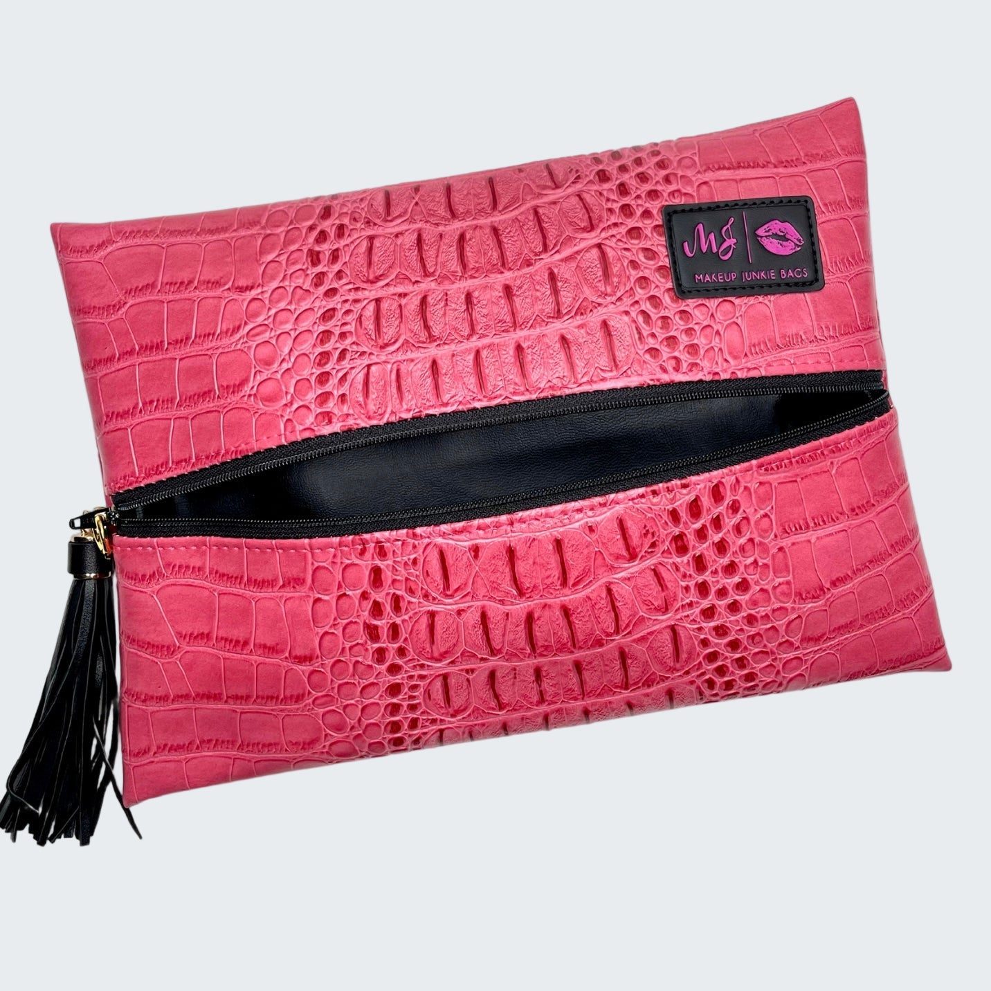 Pink crocodile-textured clutch bag with a black zipper and tassel on a white background
