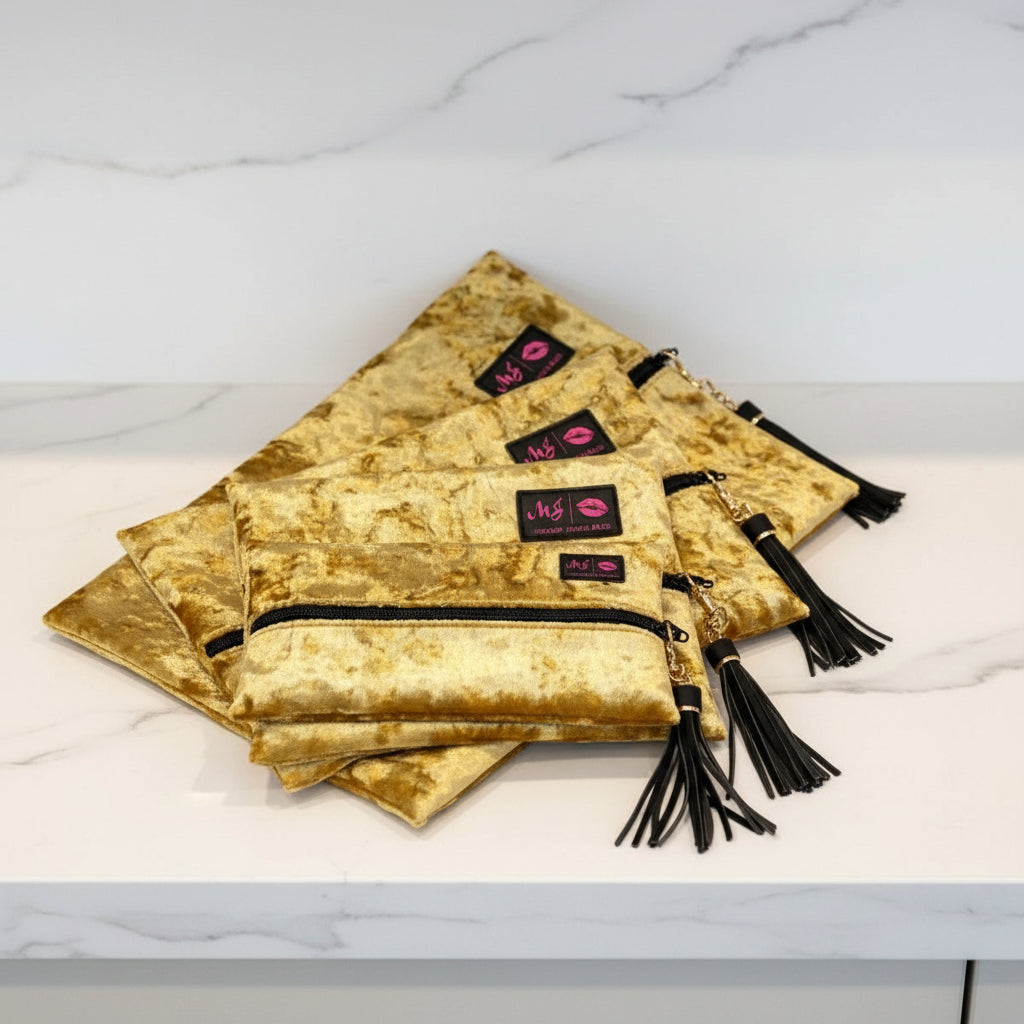Gold velvet pouches with black tassels and visible brand logo on a white background