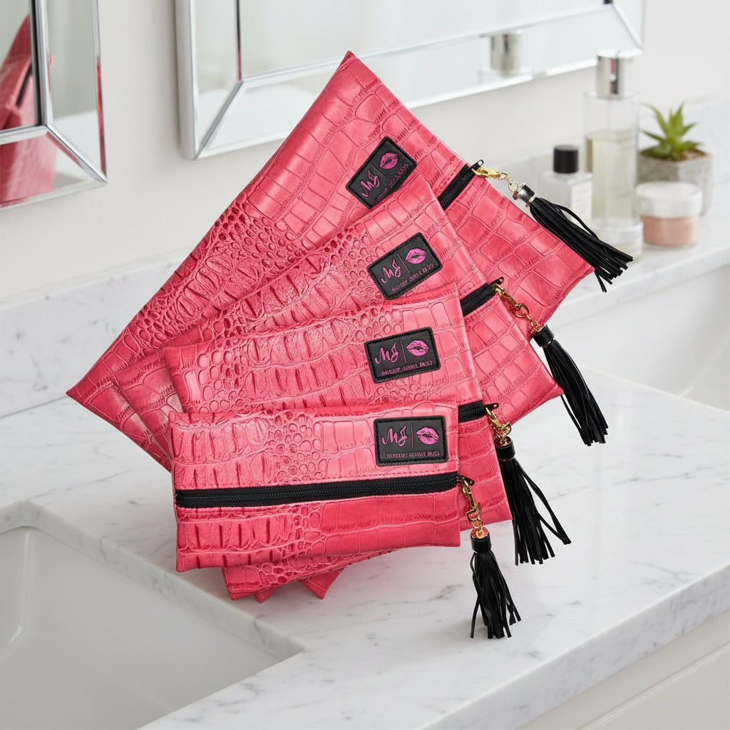 Set of pink crocodile-textured pouches with black zippers and tassels on a white background