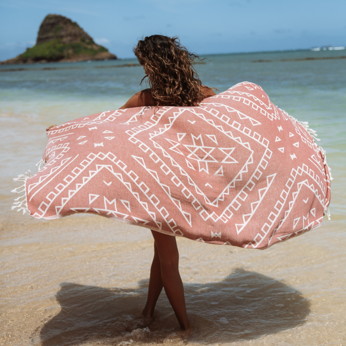 Person holding a pink and white patterned towel on a beach