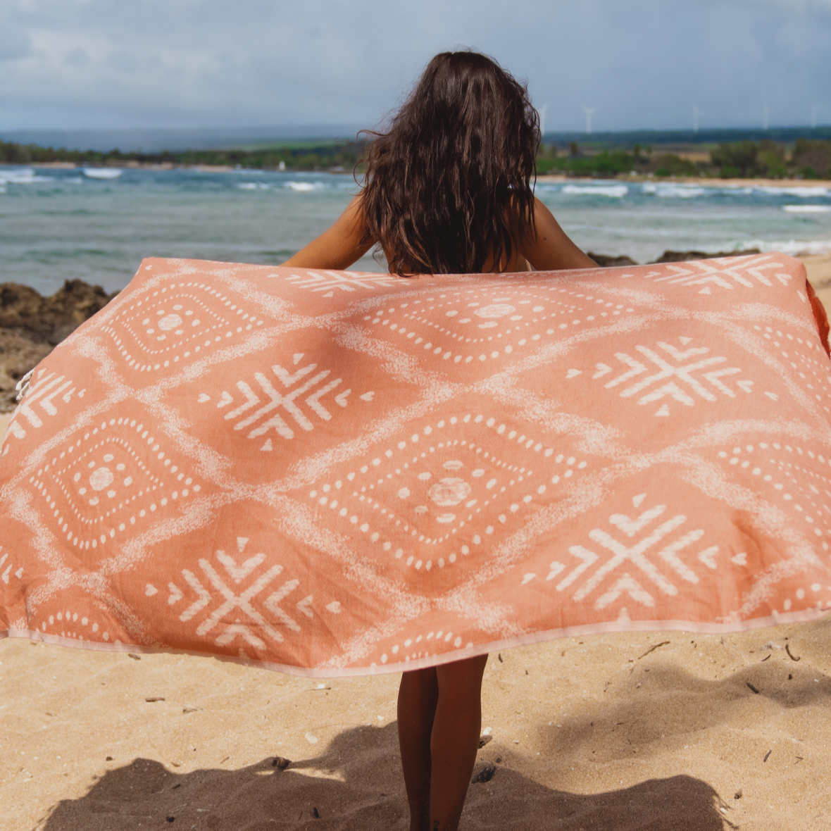 Person holding a large pink and white patterned towel on a beach
