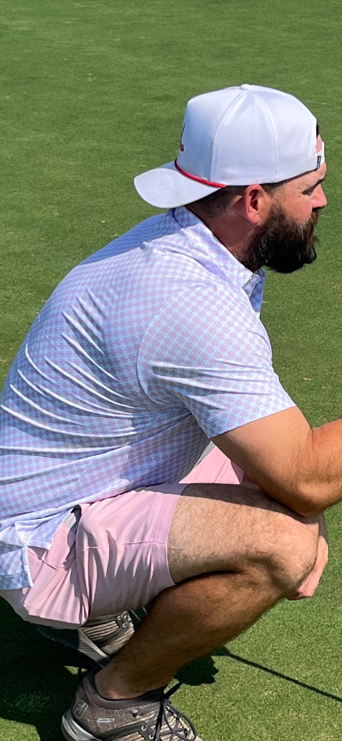 Man in light blue shirt and pink shorts crouching on a grassy field