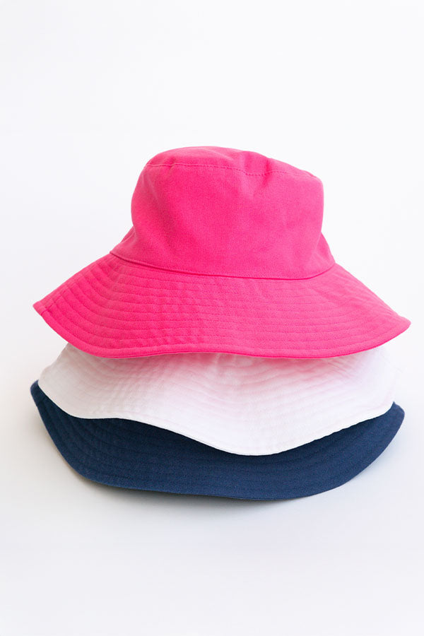 Three bucket hats in pink, white, and navy on a light gray background