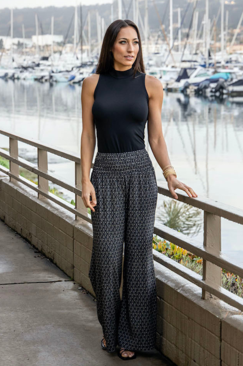 Woman standing by a marina wearing a black top and patterned pants.