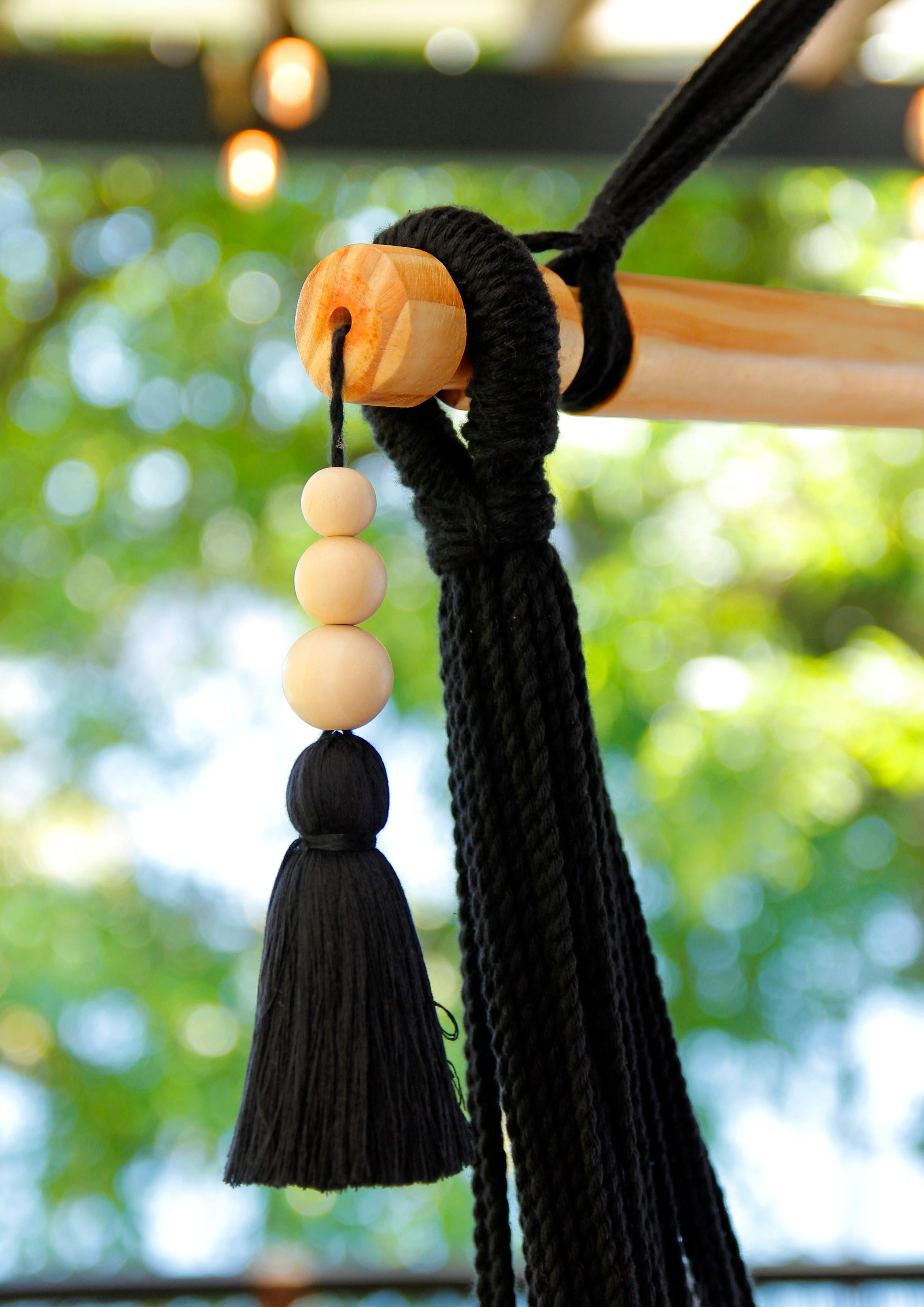 Decorative keychain with black tassels and wooden beads against a blurred natural background