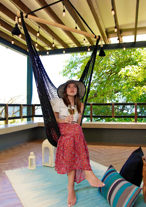 Woman in a hammock holding a glass of wine on a wooden deck with greenery in the background