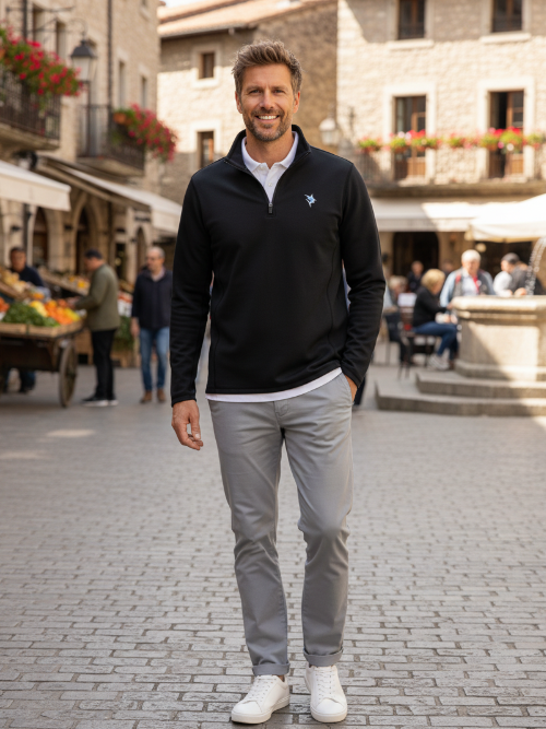 Man wearing a black quarter-zip sweater and gray pants standing on a cobblestone street.