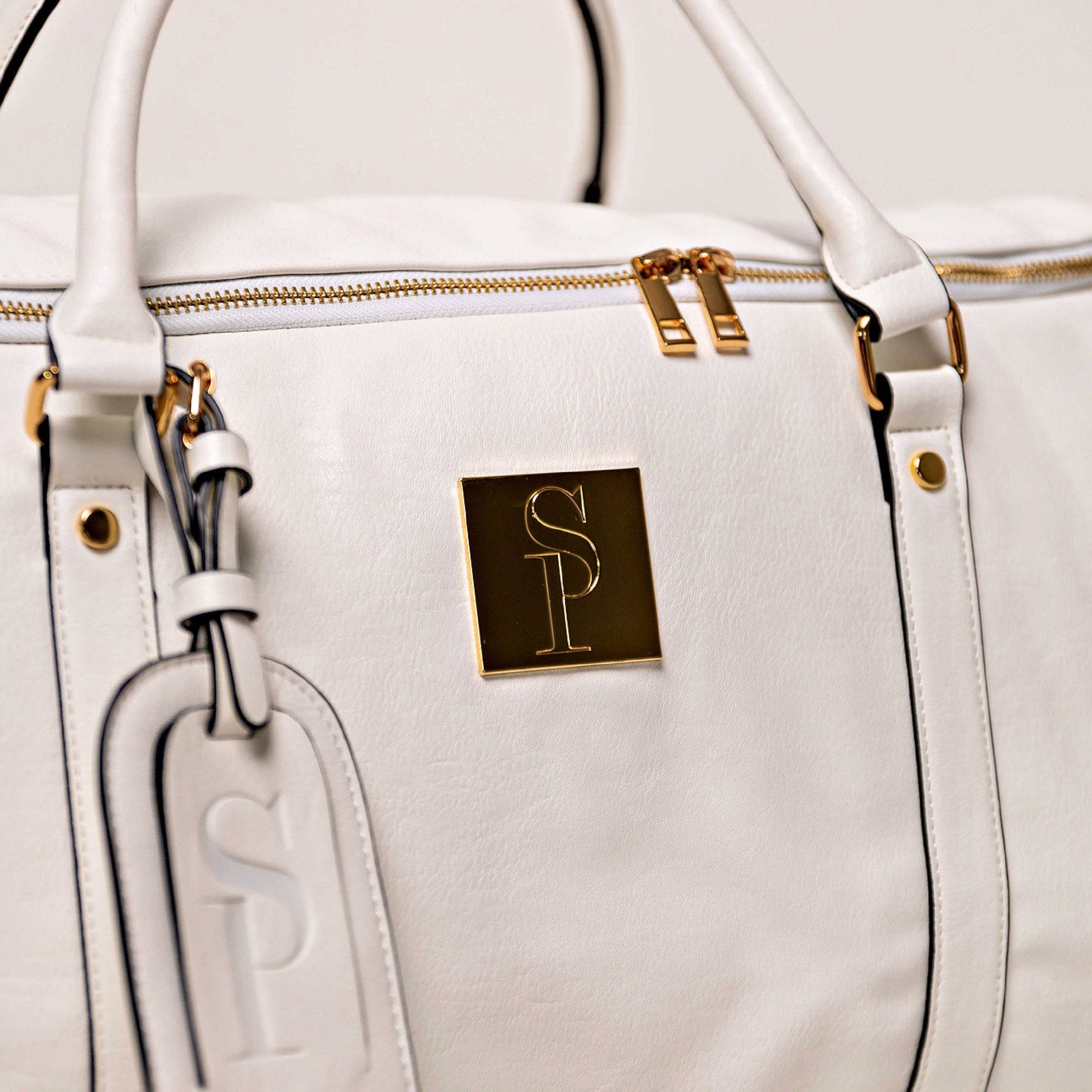 White handbag with gold accents and a logo on a light gray background