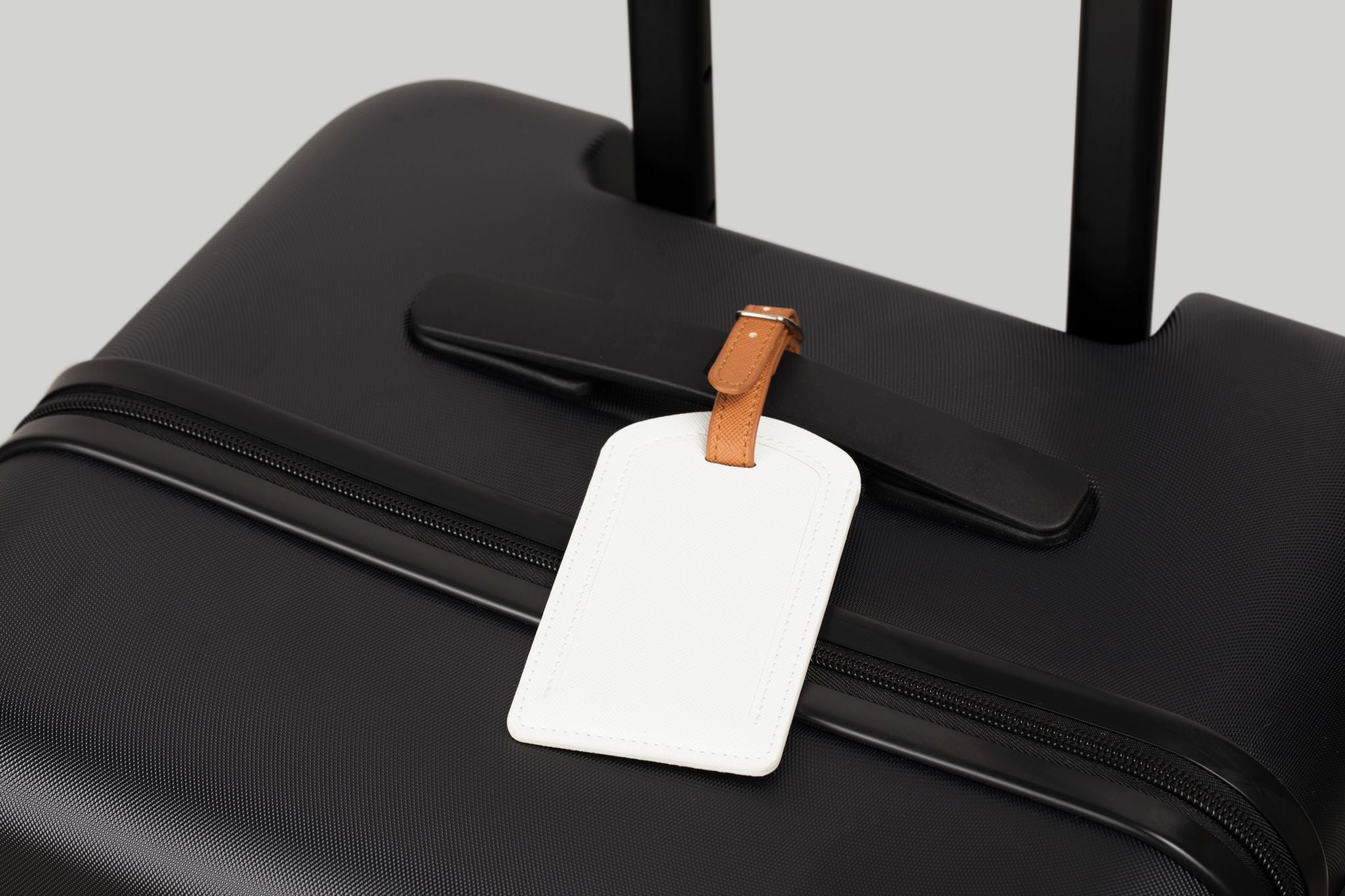 Black suitcase with a white luggage tag attached on a light gray background