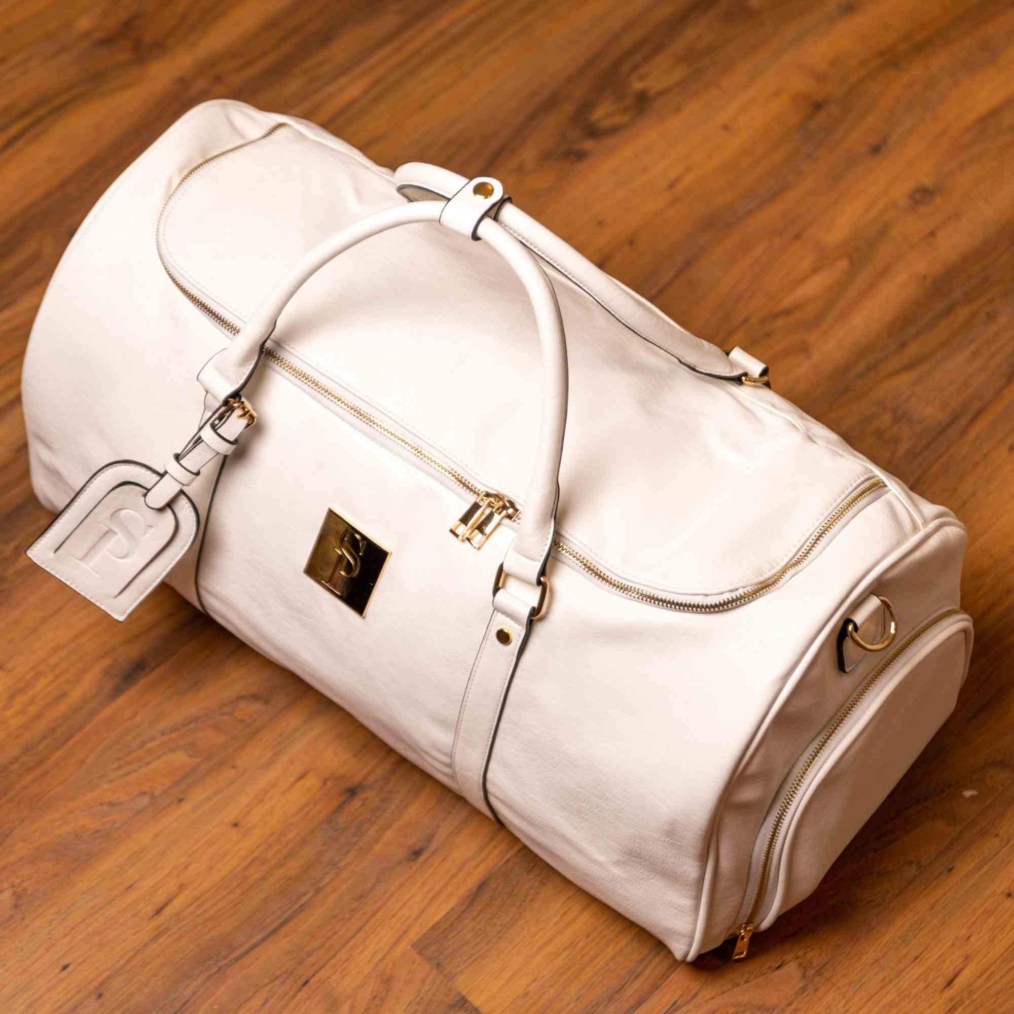 White duffel bag with gold accents on a wooden floor