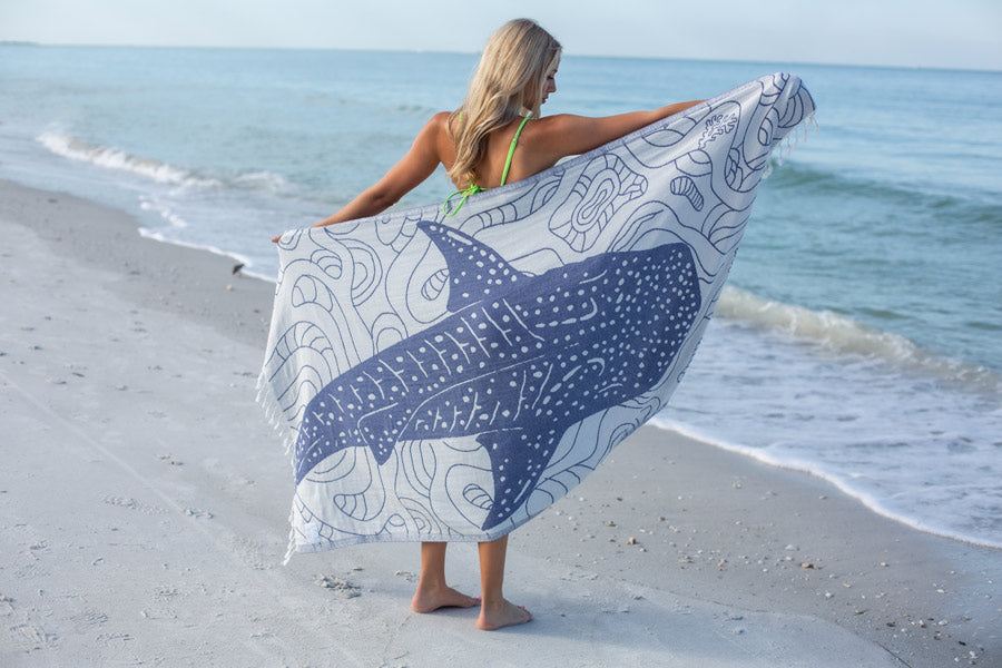 Woman on a beach holding a towel with a whale design