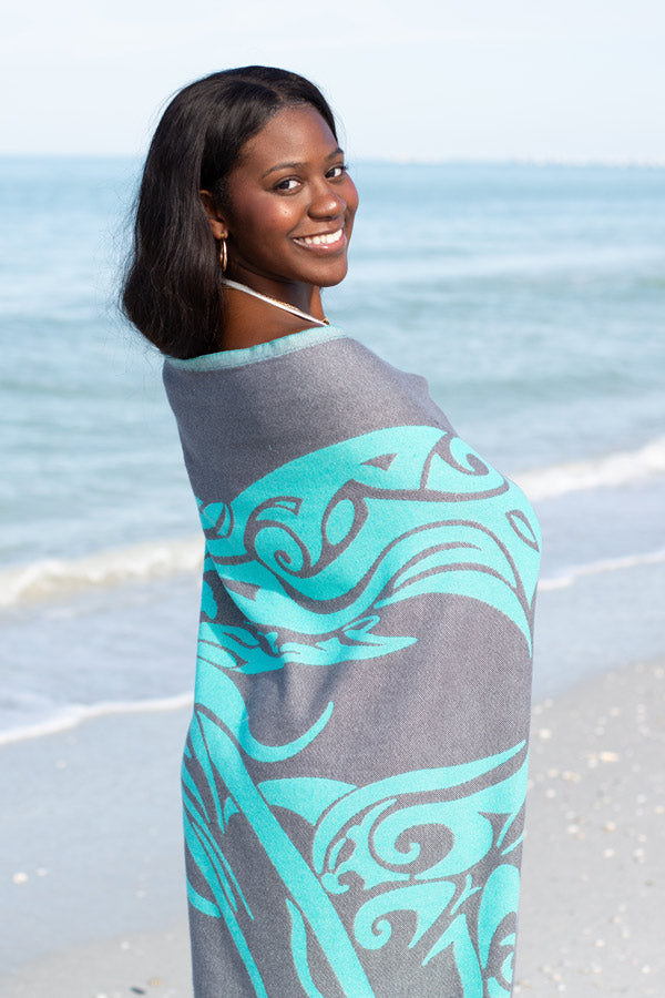 Woman on a beach wearing a gray and teal patterned cover-up.