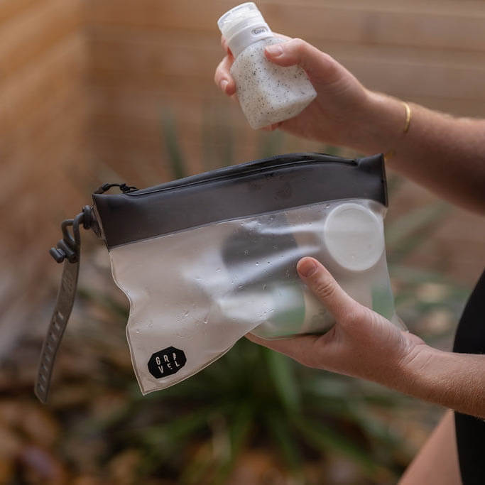 Person holding a clear pouch with a black zipper and a bottle of sandalwood-scented salt.
