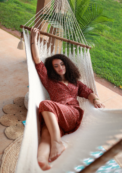 Woman in a red dress relaxing in a white hammock with greenery in the background