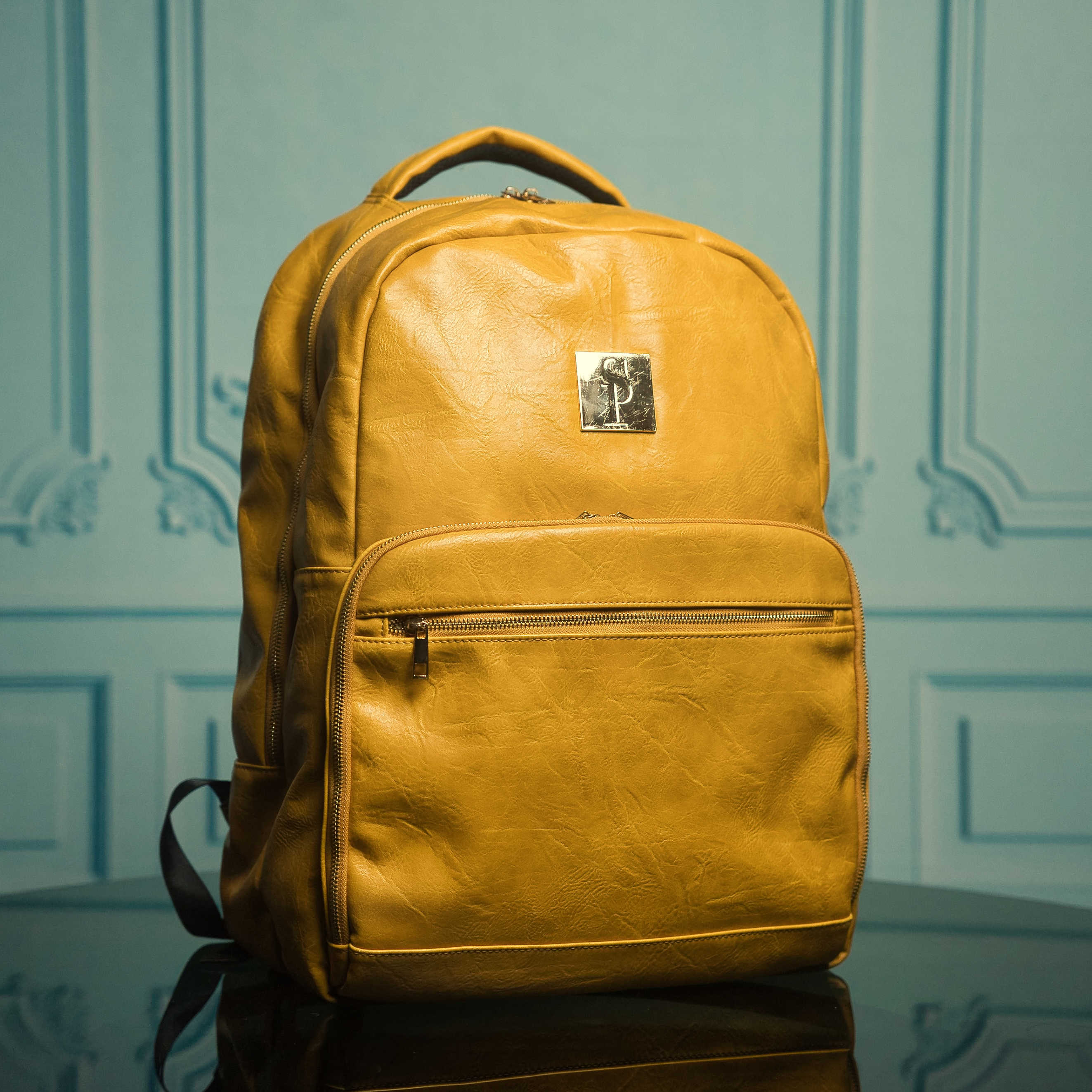 Yellow backpack with a brand logo on a reflective surface and light blue wall background