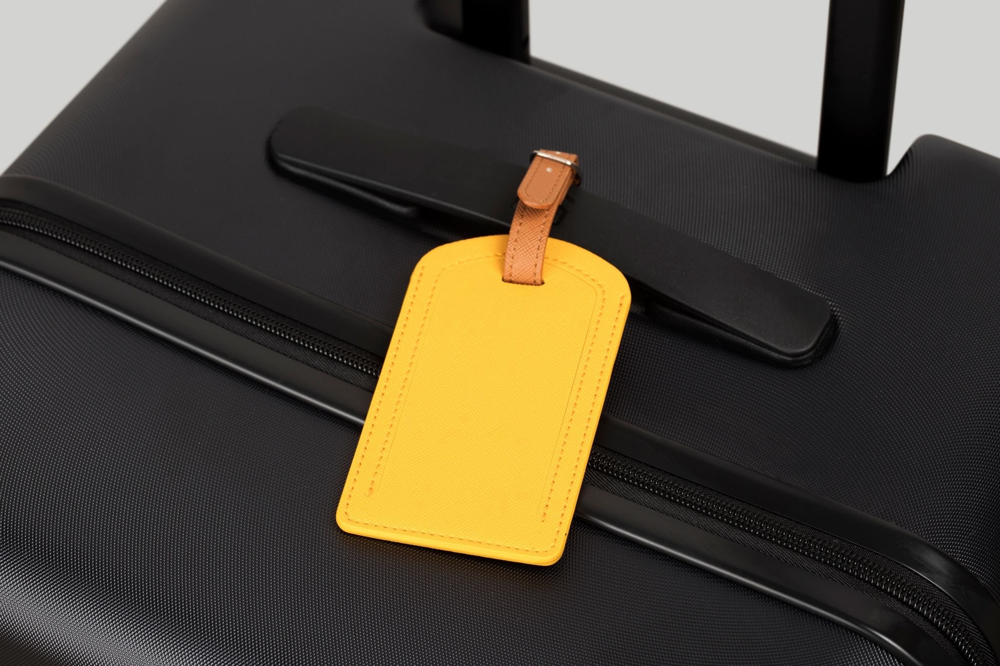 Black suitcase with a yellow luggage tag on a light gray background