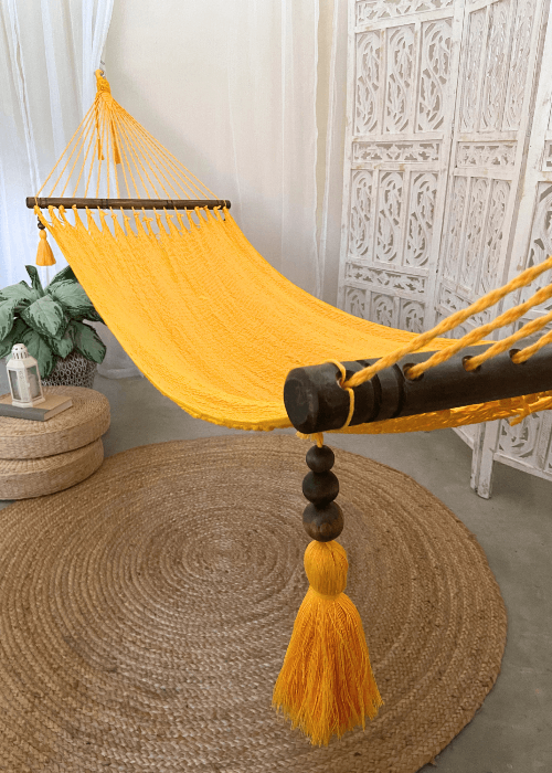 Yellow hammock with wooden frame and tassels on a textured rug