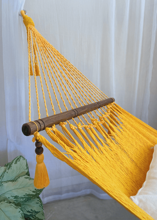 Yellow hammock with wooden rod and tassels against a white curtain background