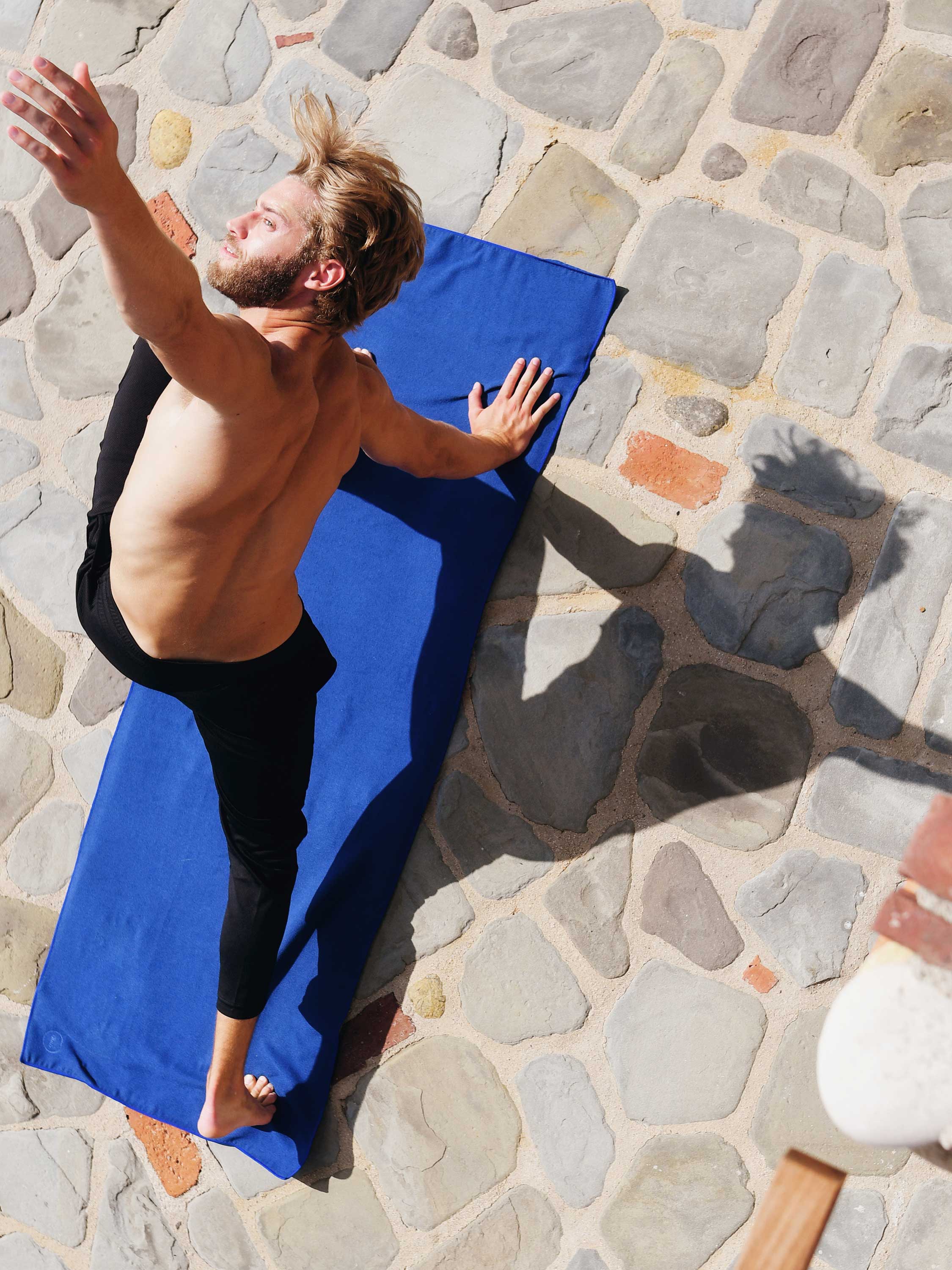 Man lying on a blue towel on a stone pavement
