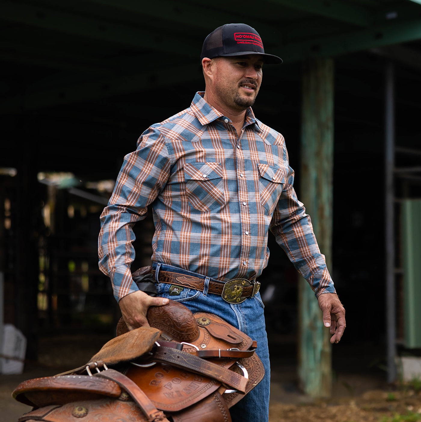 Man carrying a leather saddle in an outdoor setting
