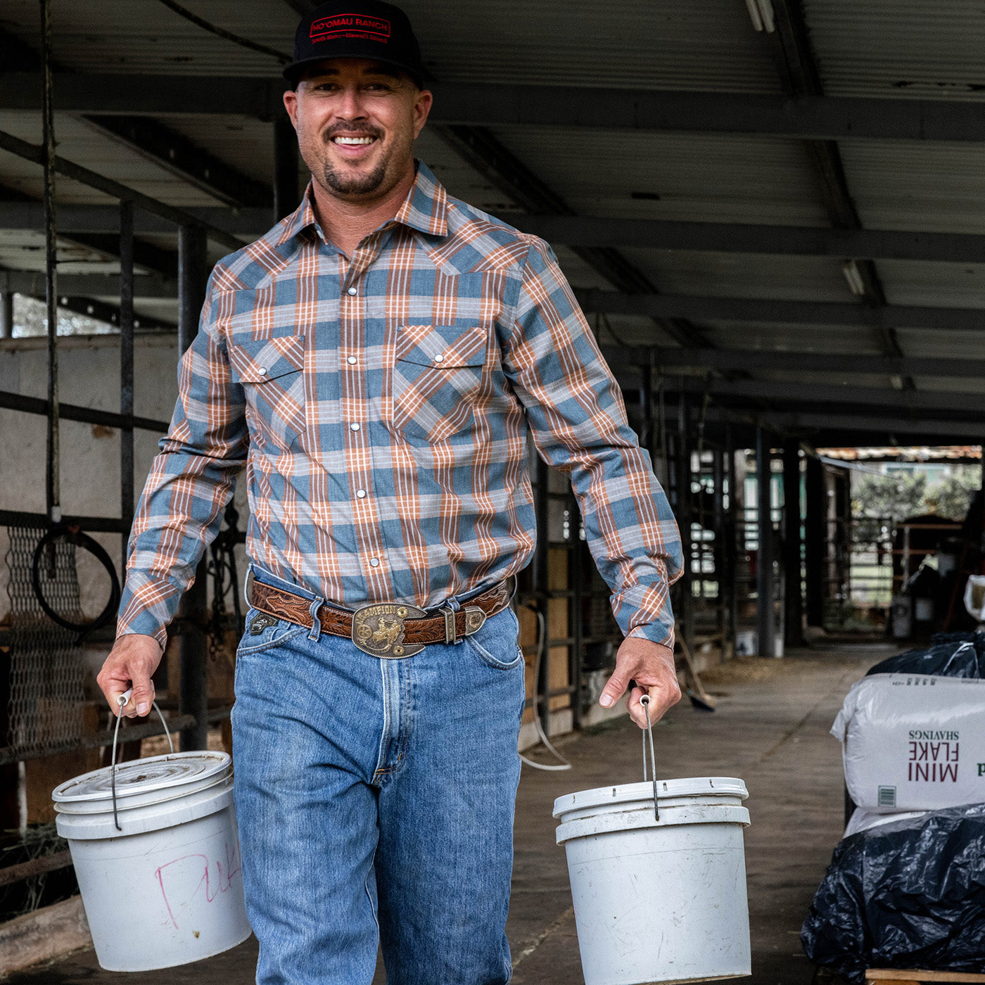 Man in plaid shirt and jeans holding two buckets in an indoor setting
