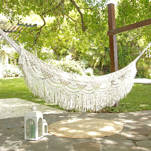 White macrame hammock in a garden setting with trees and a lantern.