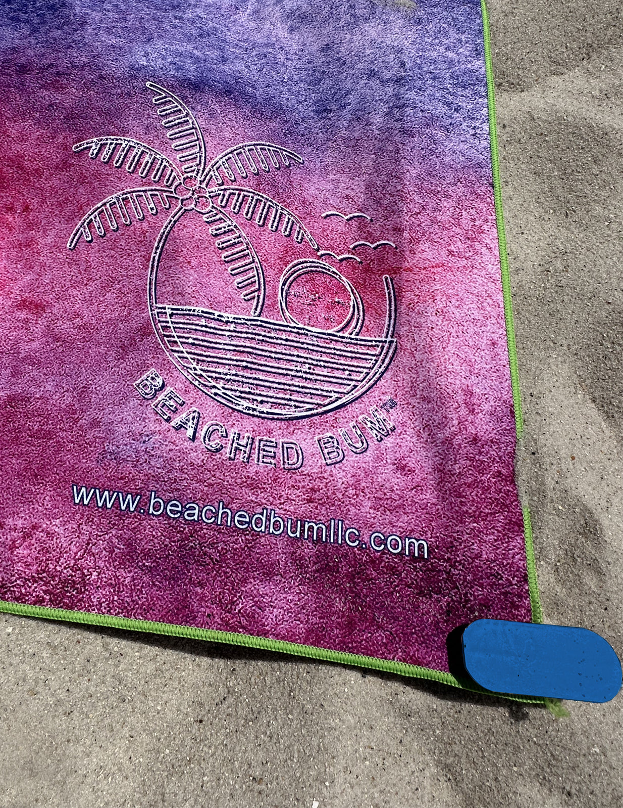 Purple towel with 'Beached Bum' logo on a sandy surface