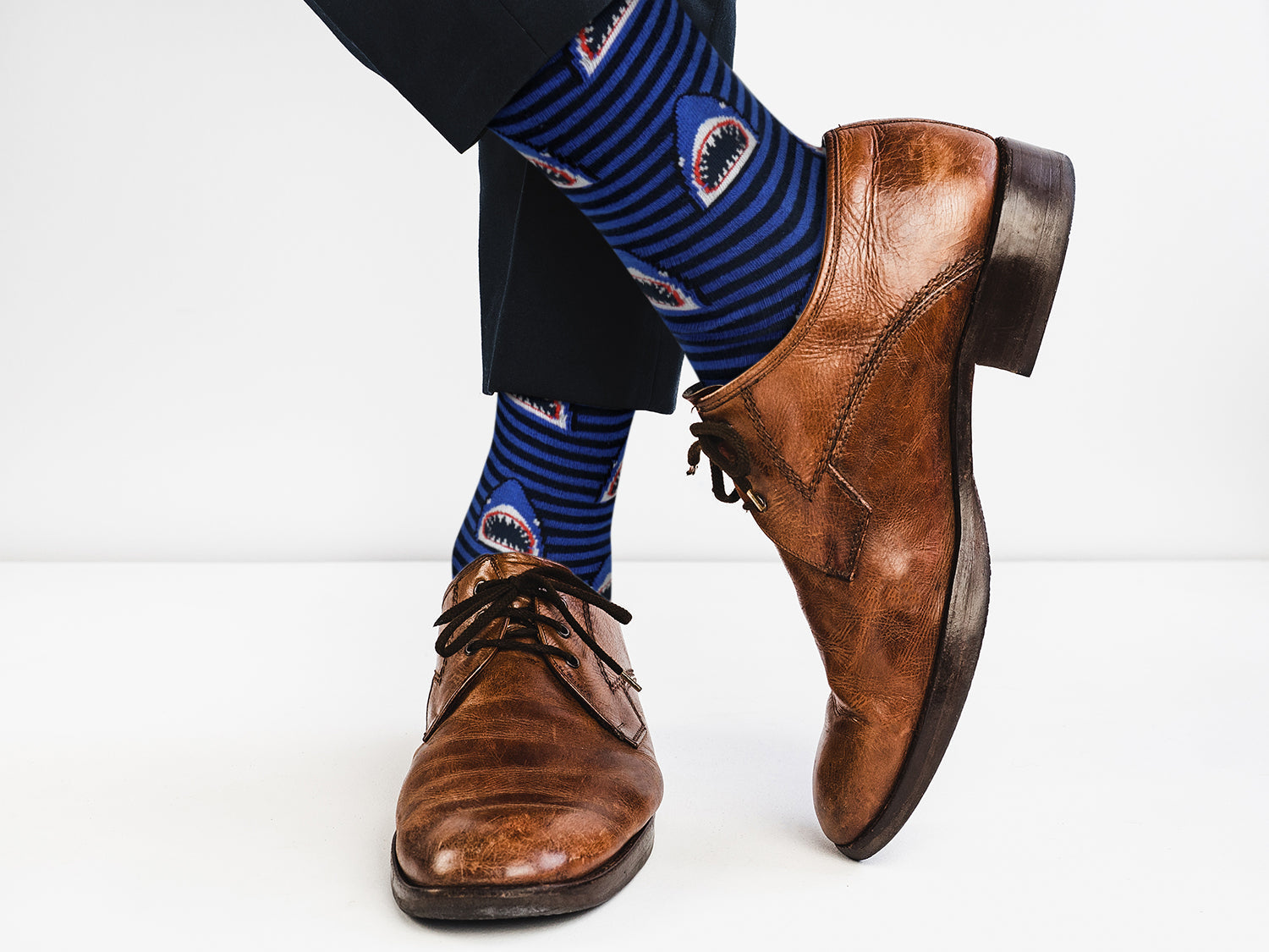 Brown leather shoes and blue socks with shark design on a white background