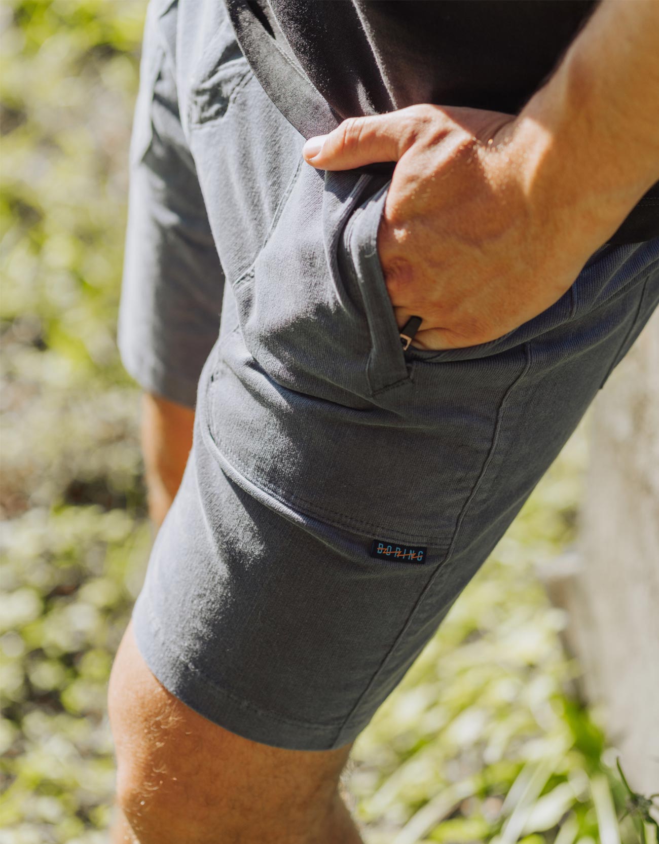 Person wearing gray shorts with a brand logo, standing outdoors.