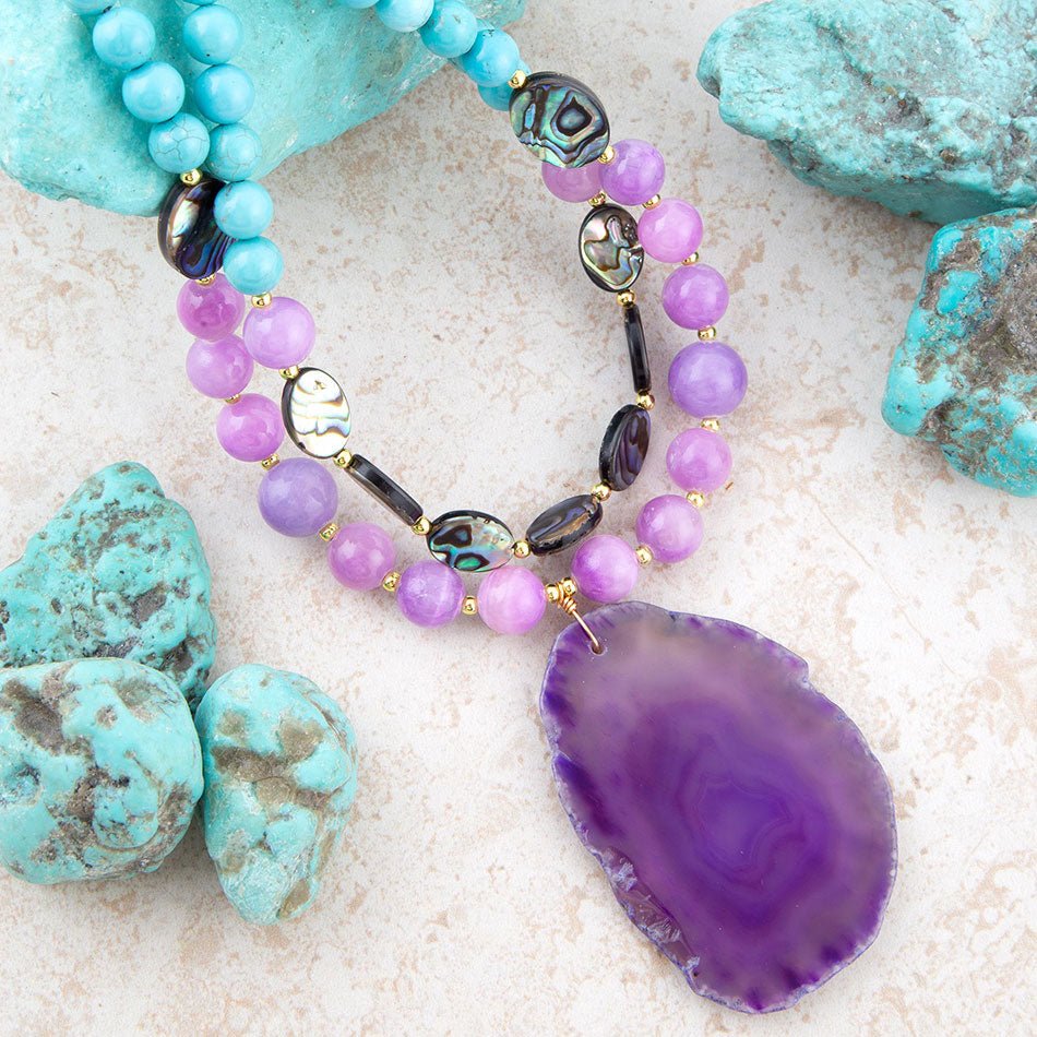 Beaded bracelet with purple and black stones on a textured surface with turquoise stones.