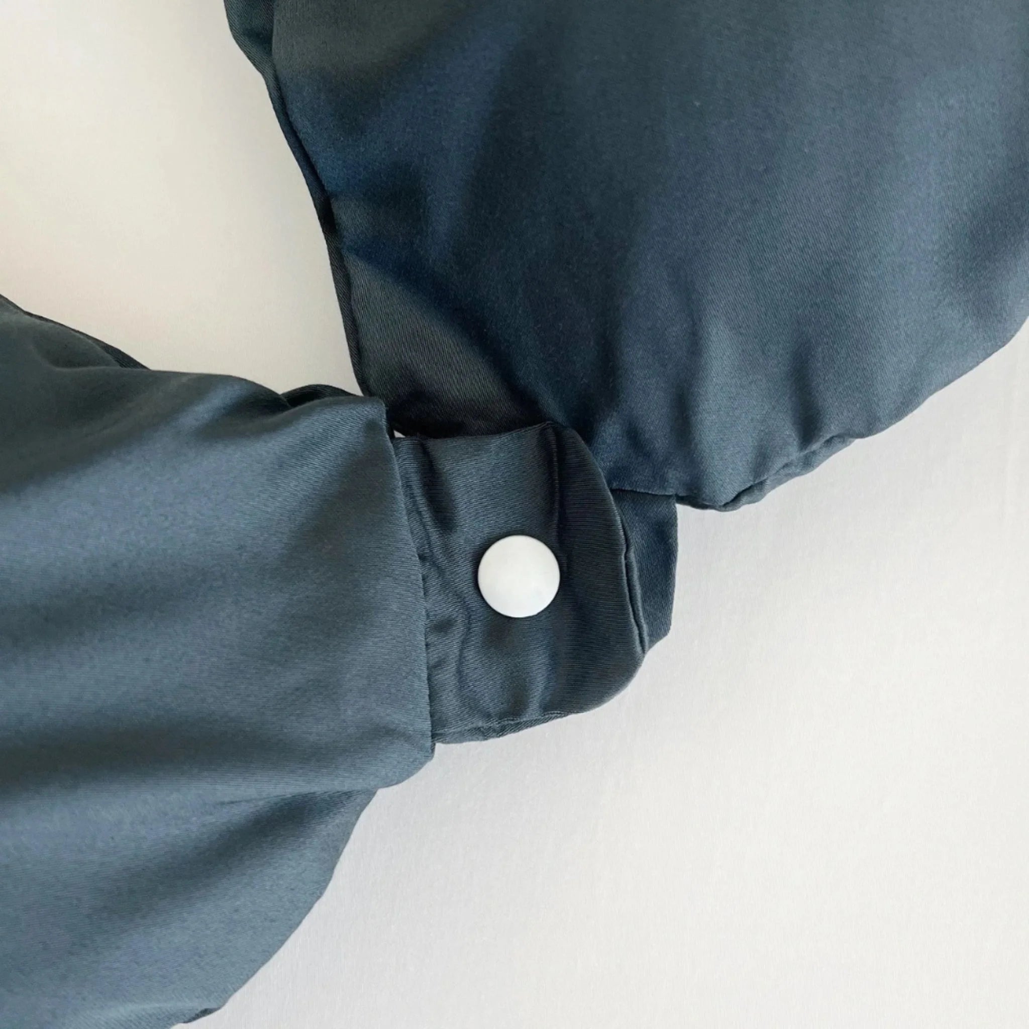 Close-up of a dark blue sleeve with a white button on a light gray background