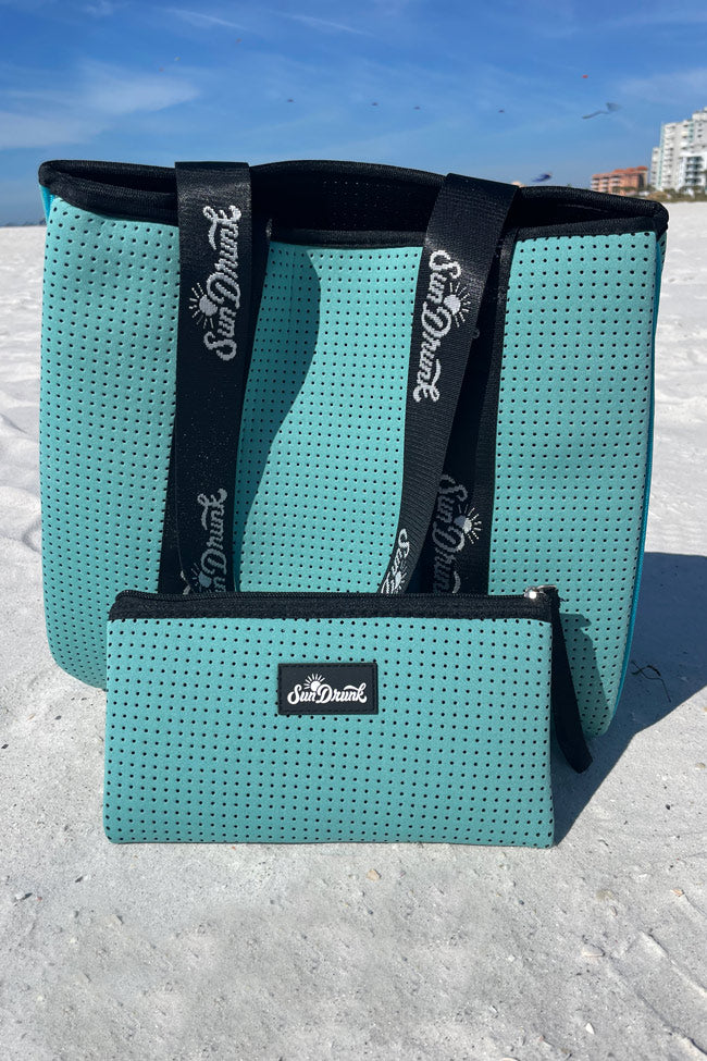 Teal perforated bag with black straps on a sandy beach