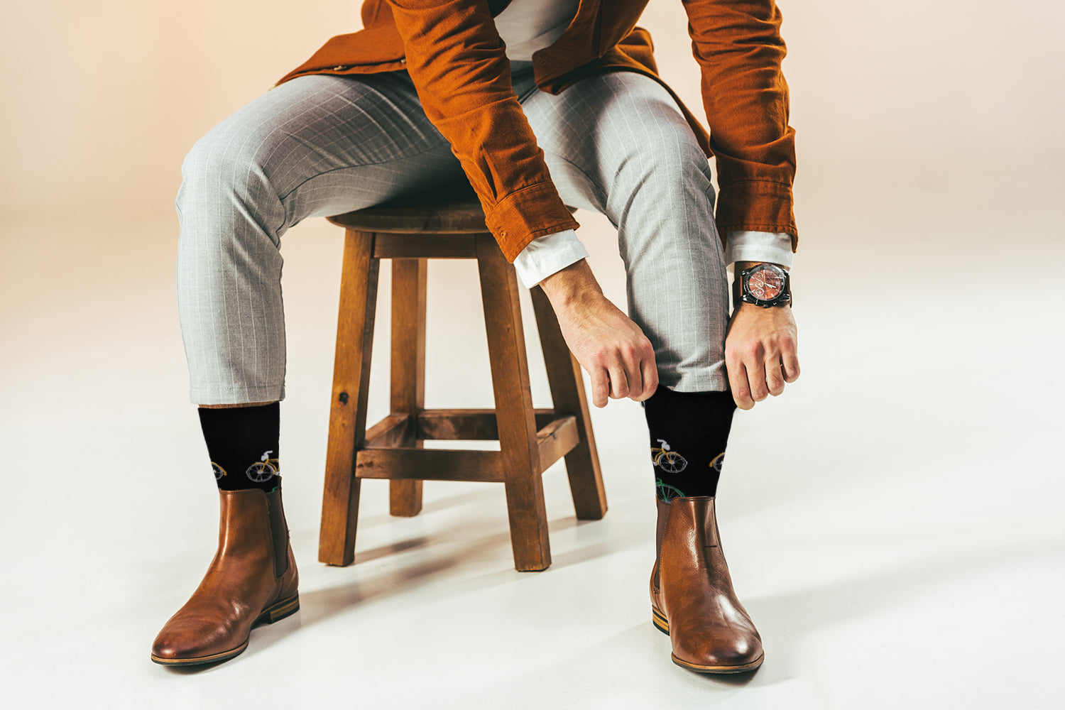 Person wearing brown leather boots, light gray pants, and a brown jacket sitting on a wooden stool.