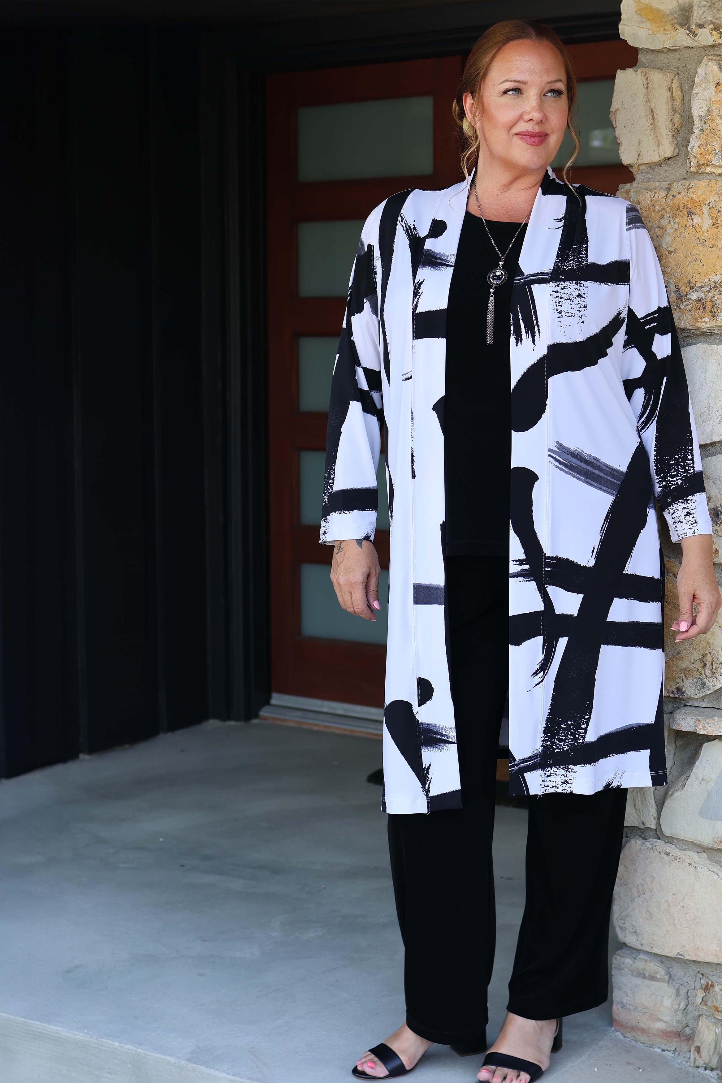Woman wearing a black and white patterned coat standing in front of a stone wall.