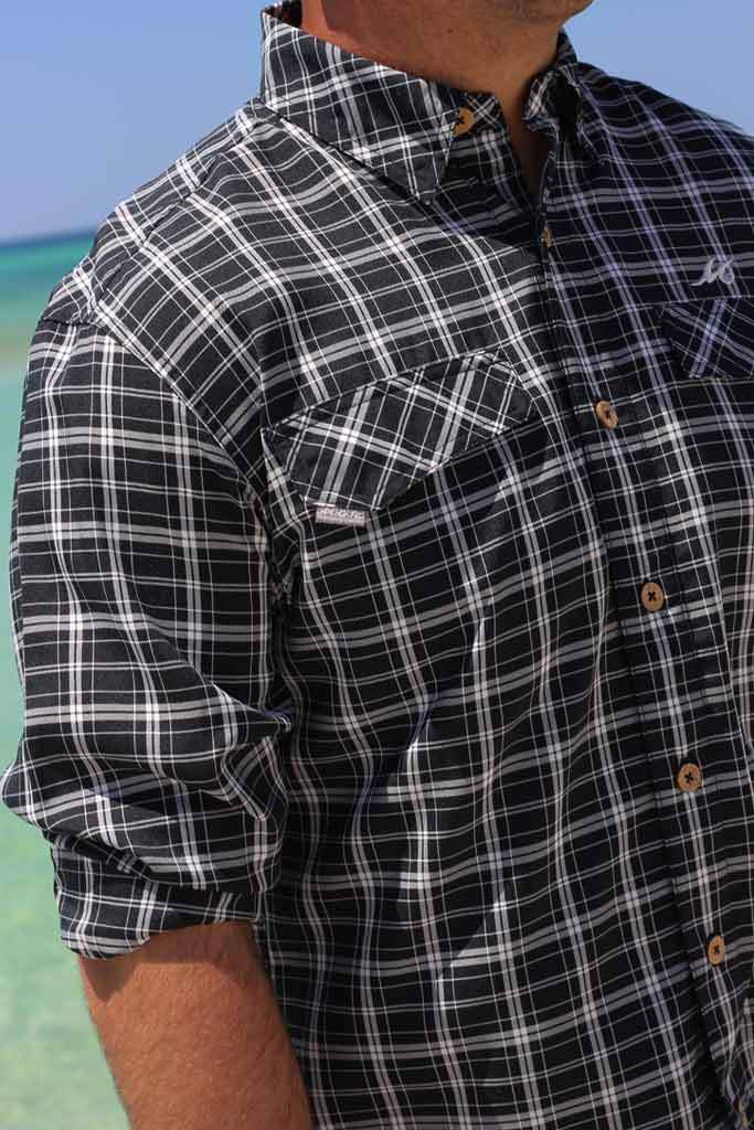 Person wearing a black and white plaid shirt with a blurred beach background