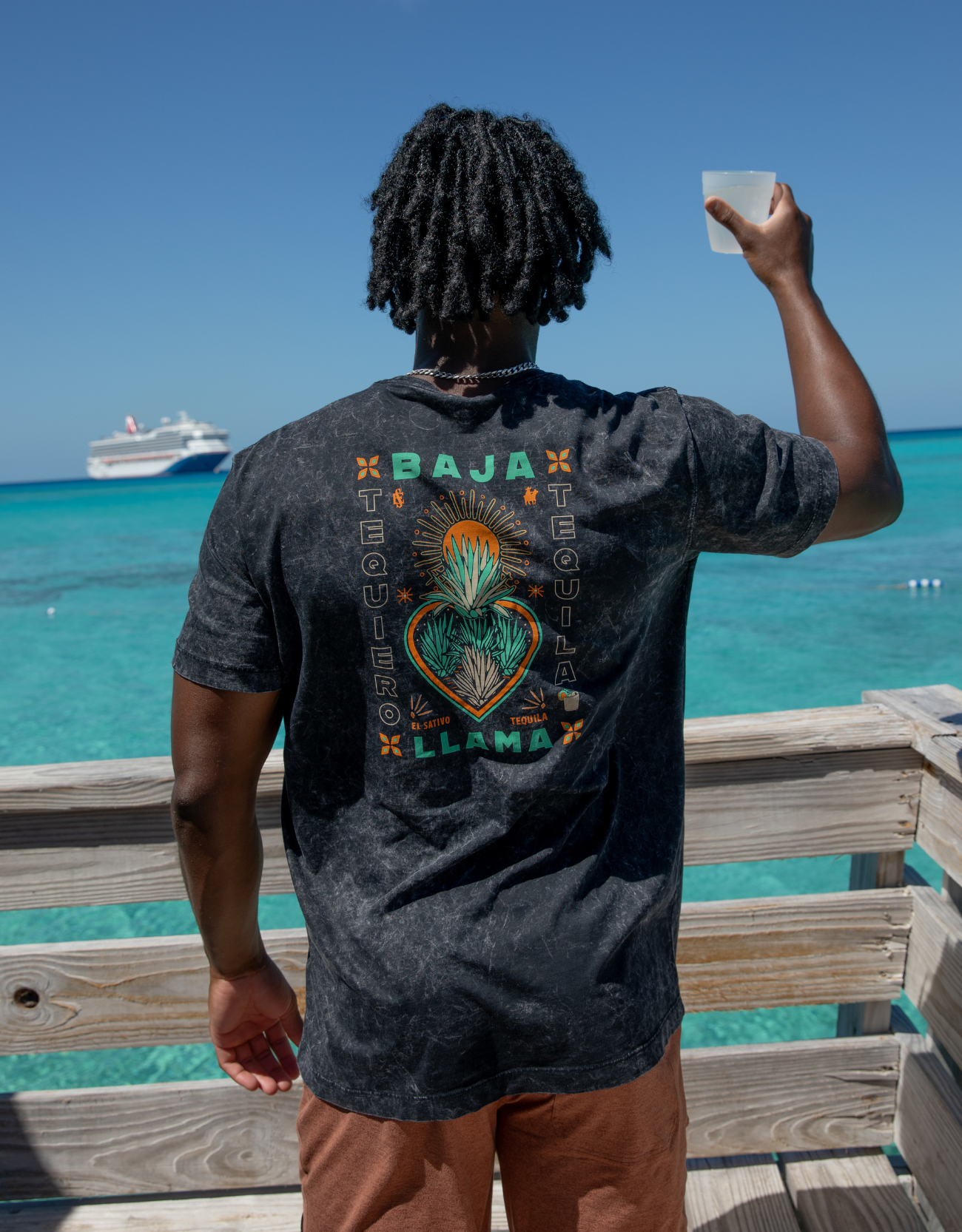 Person wearing a t-shirt with 'Baja Llama' design by the ocean