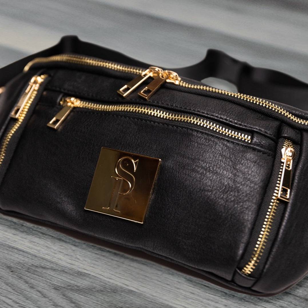 Black leather bag with gold zippers and logo on a gray surface