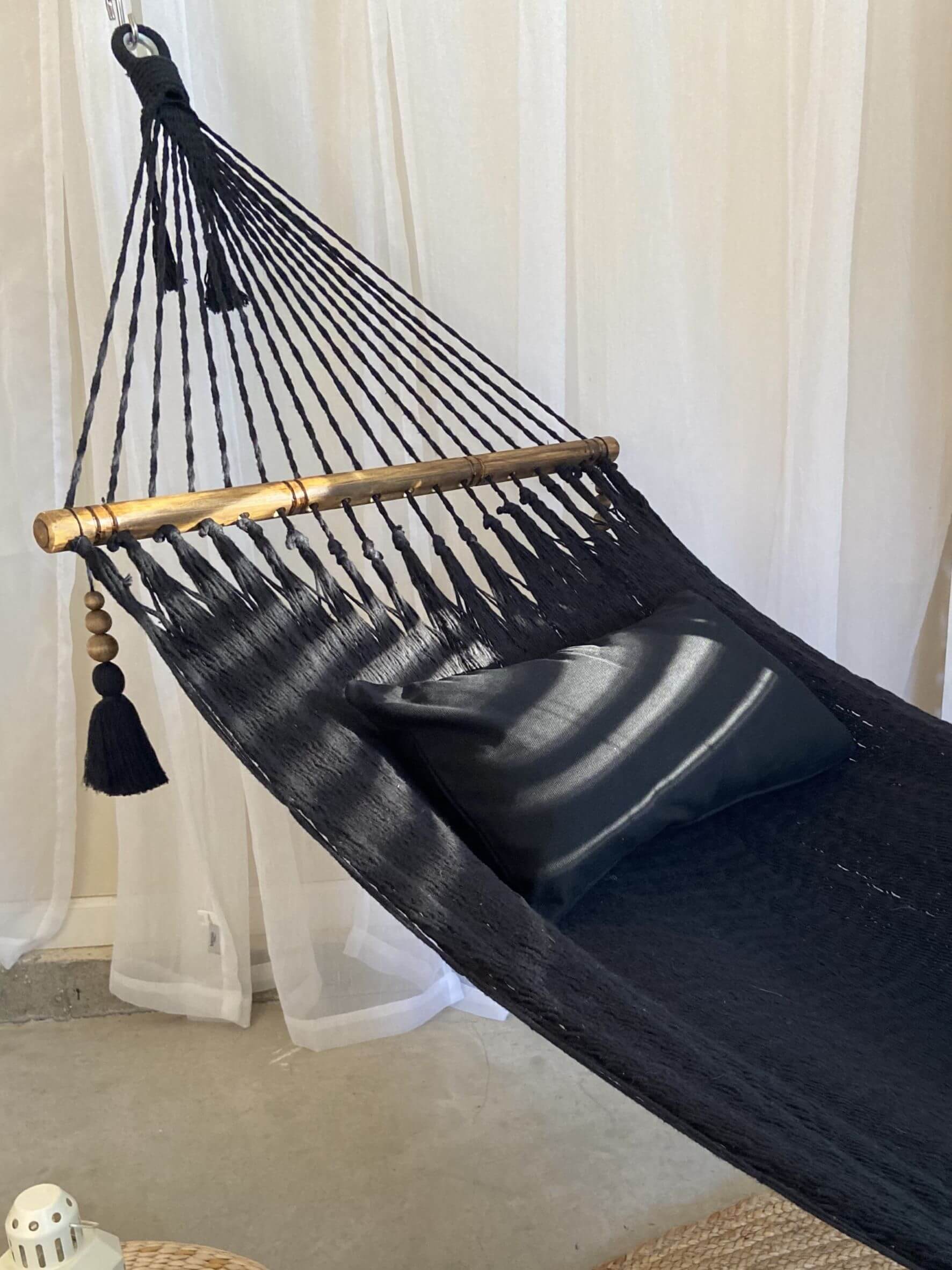 Black hammock with gold accents and tassels against a white curtain background
