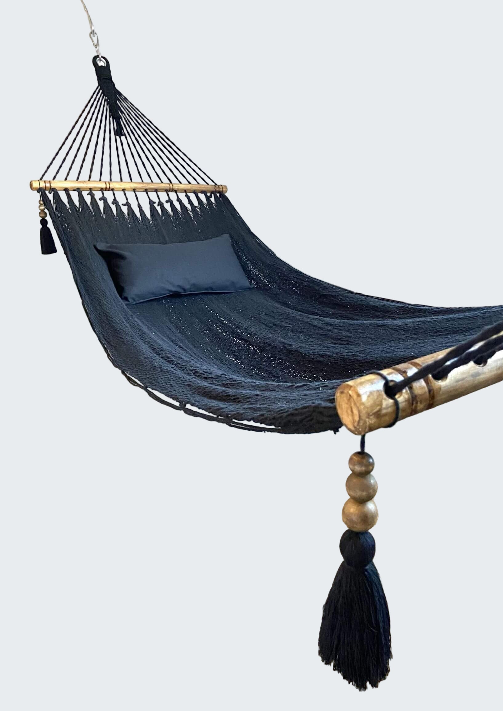 Navy blue hammock with wooden poles and tassels in a room with a textured rug and decorative wall.