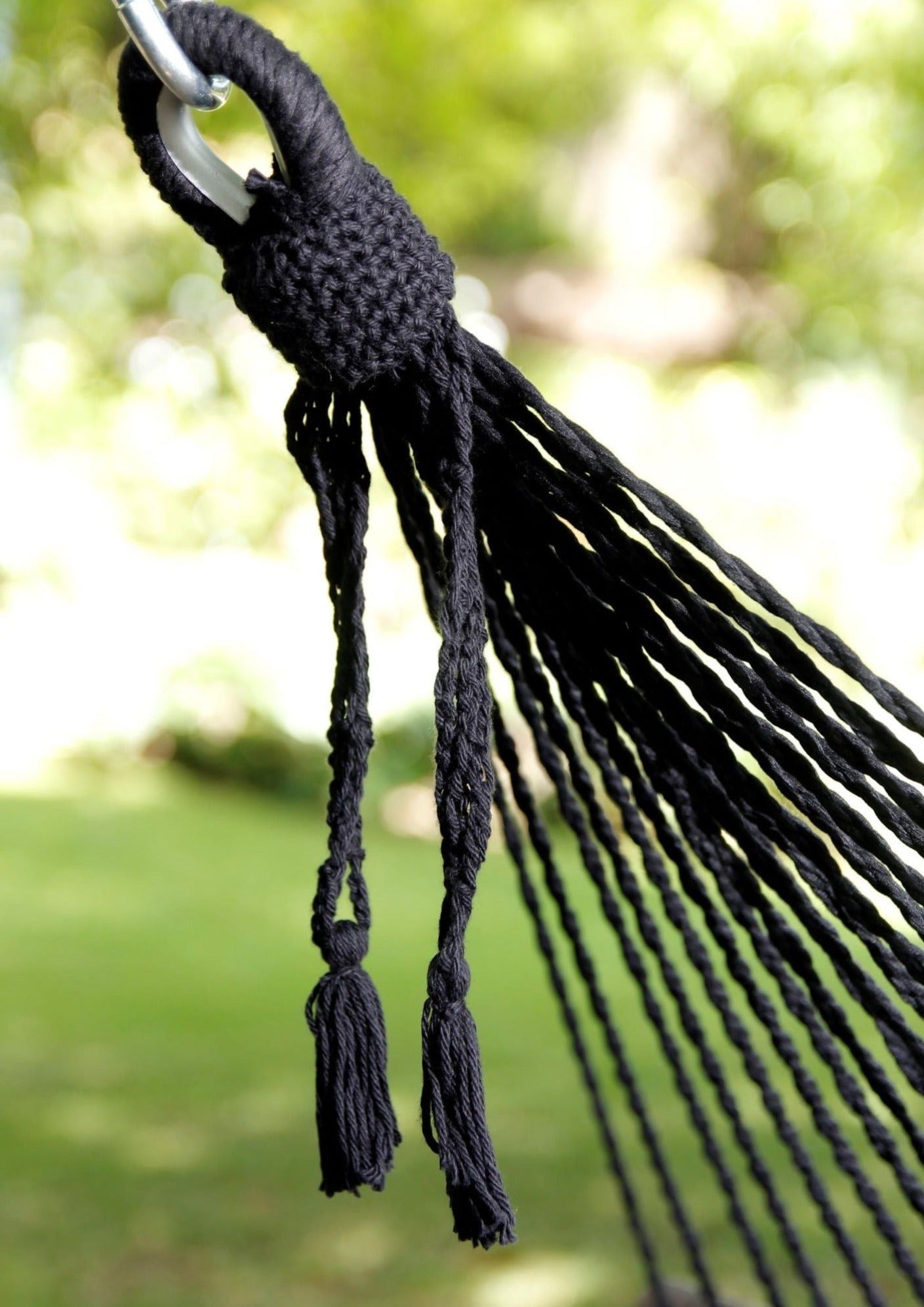 Close-up of a black hammock with tassels against a blurred green outdoor background