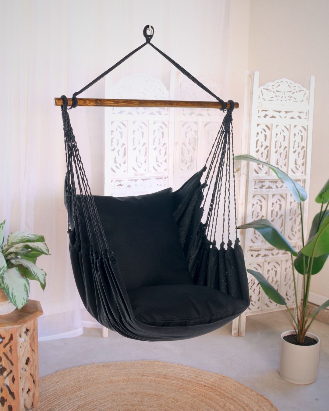 Black hammock chair in a room with plants and a decorative screen.