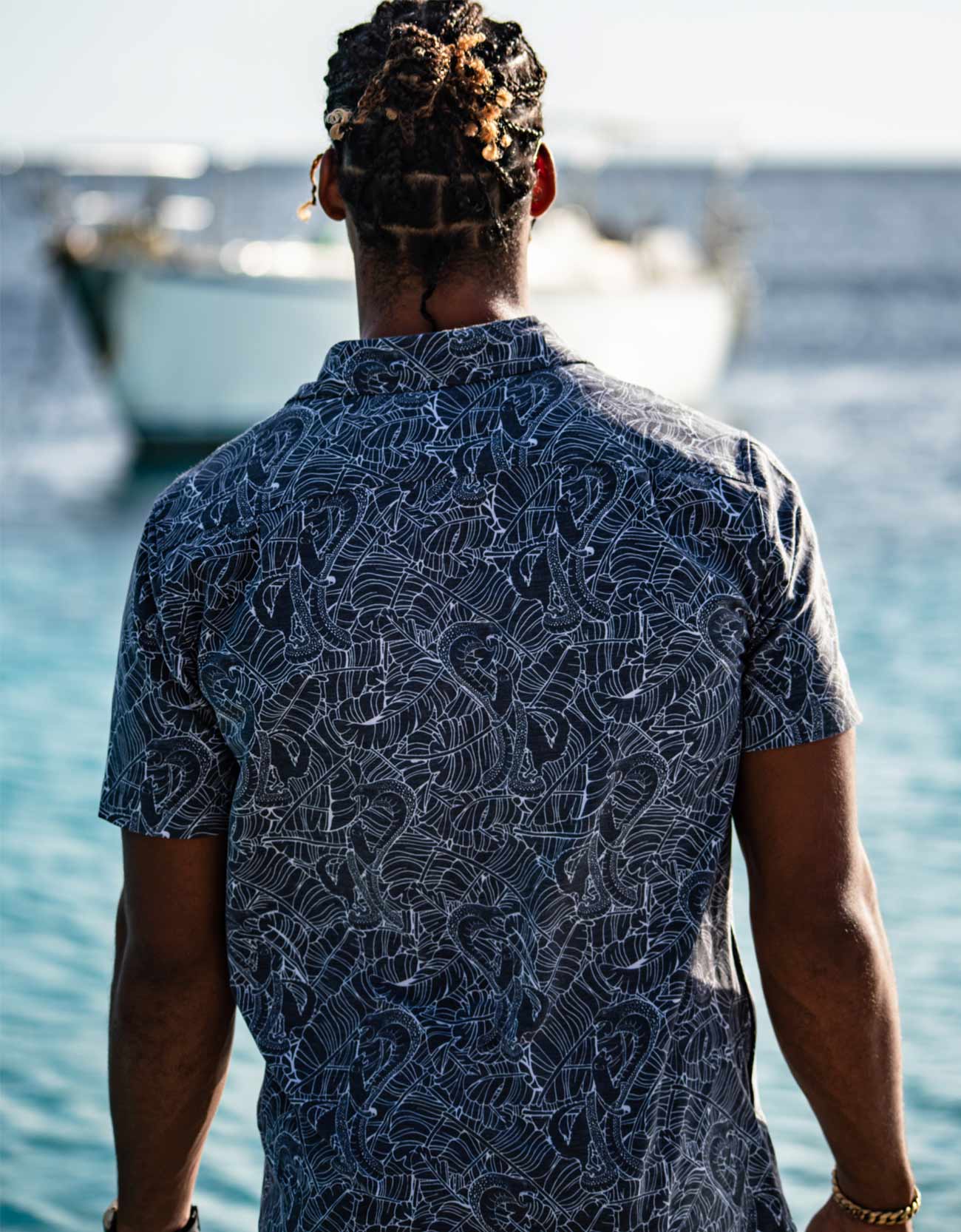 Person wearing a patterned shirt standing by the water with boats in the background