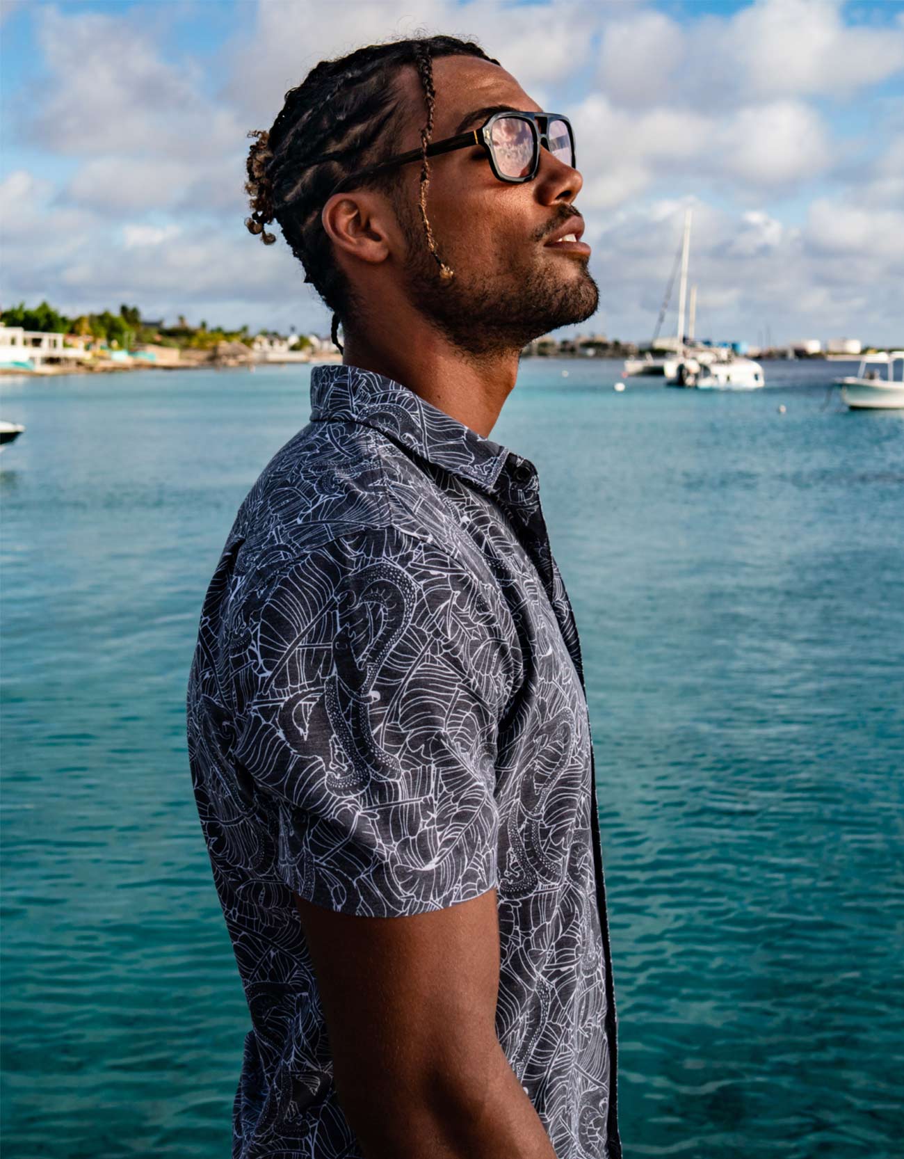Man with glasses standing by a waterfront with boats and a clear sky.