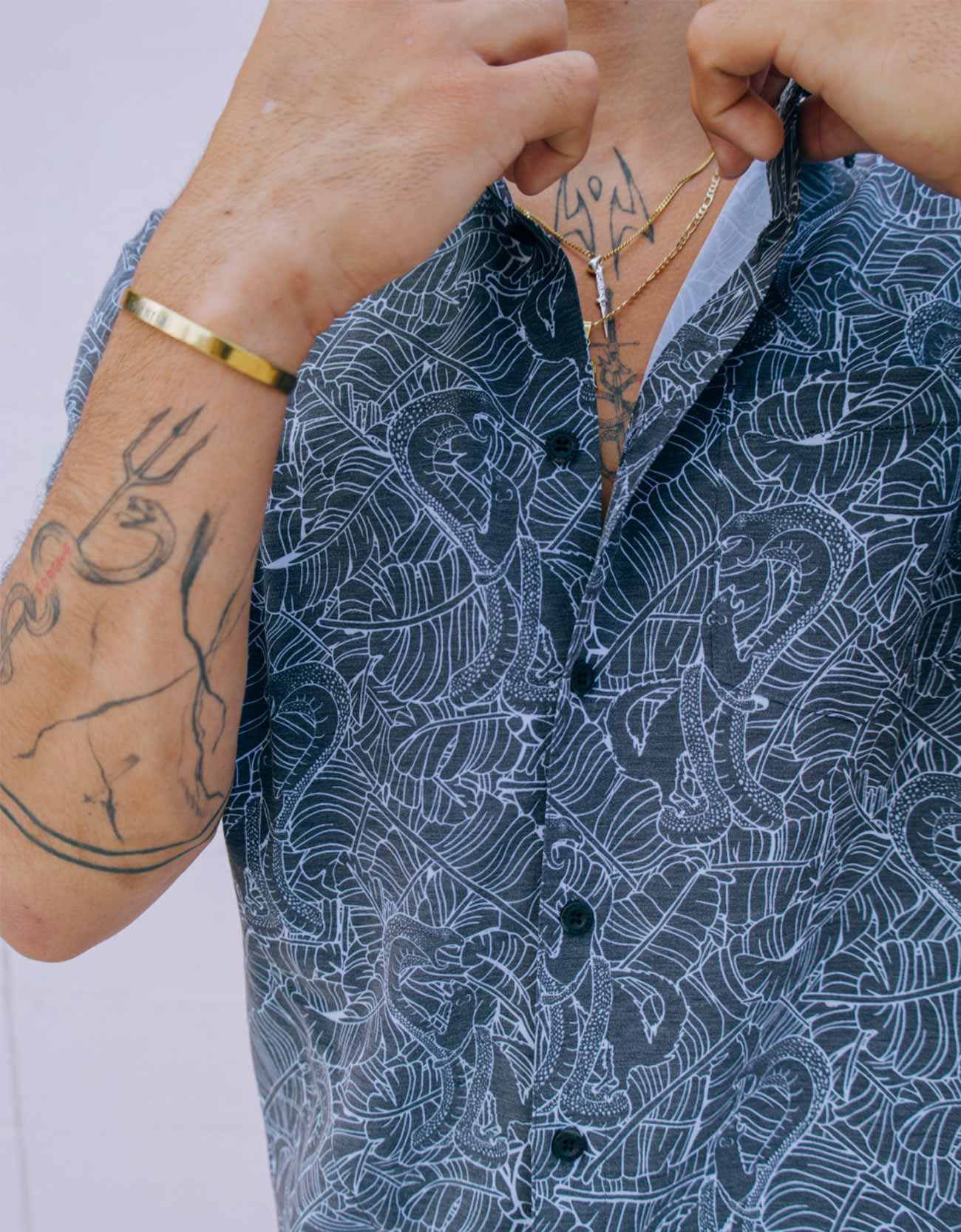 Person wearing a blue patterned shirt with visible tattoos on arms and neck.