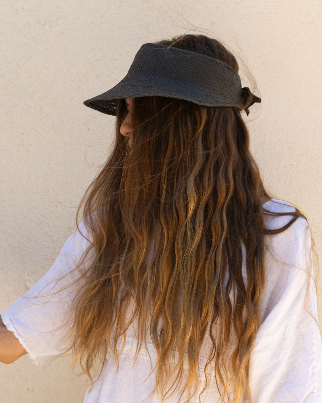 Person wearing a black visor with long wavy hair against a beige wall