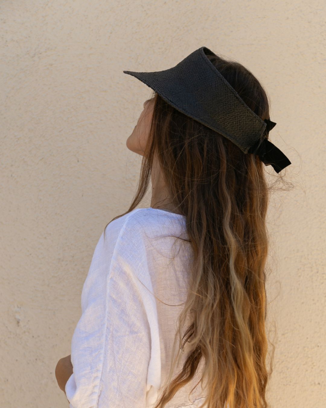 Person wearing a black visor with a bow on a beige background