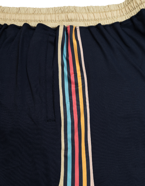 Black pants with colorful striped side panels on a beige background