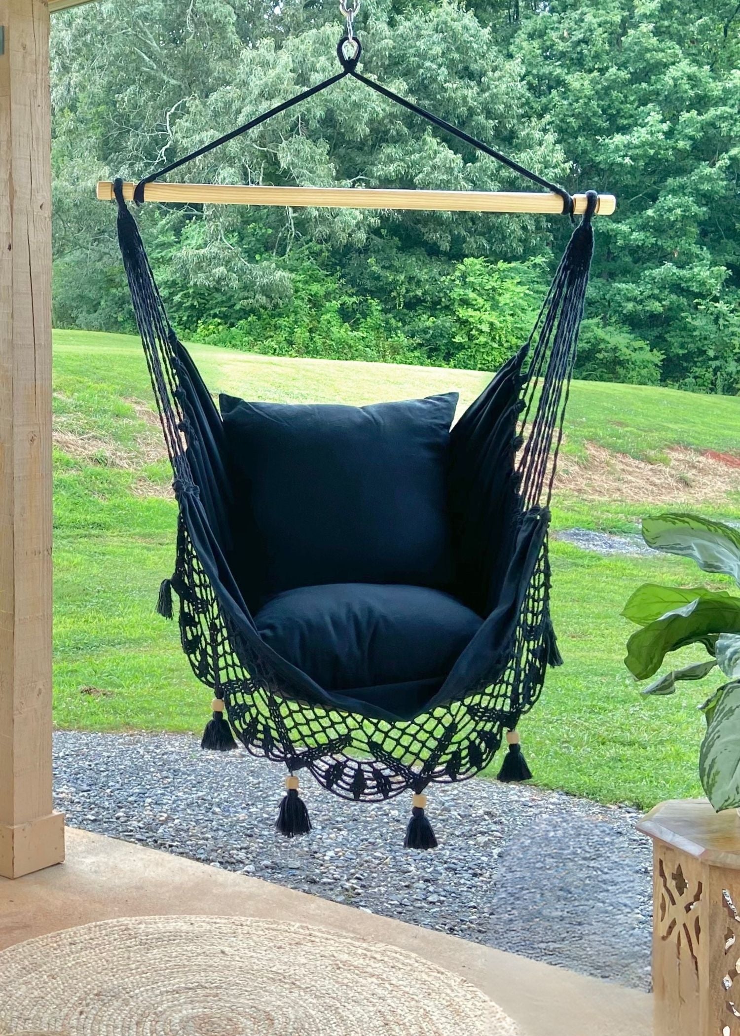 Black hammock chair with cushions hanging outdoors on a wooden stand.