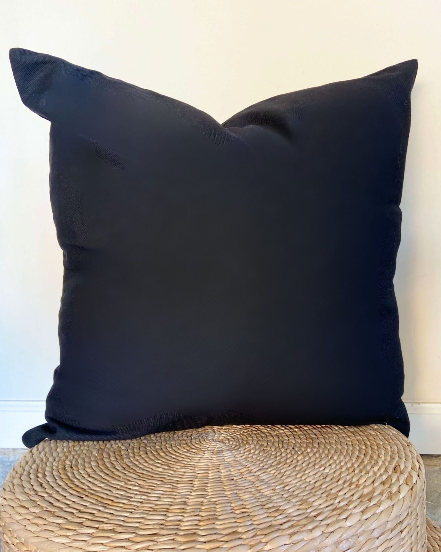 Black pillow on a woven stool against a white wall