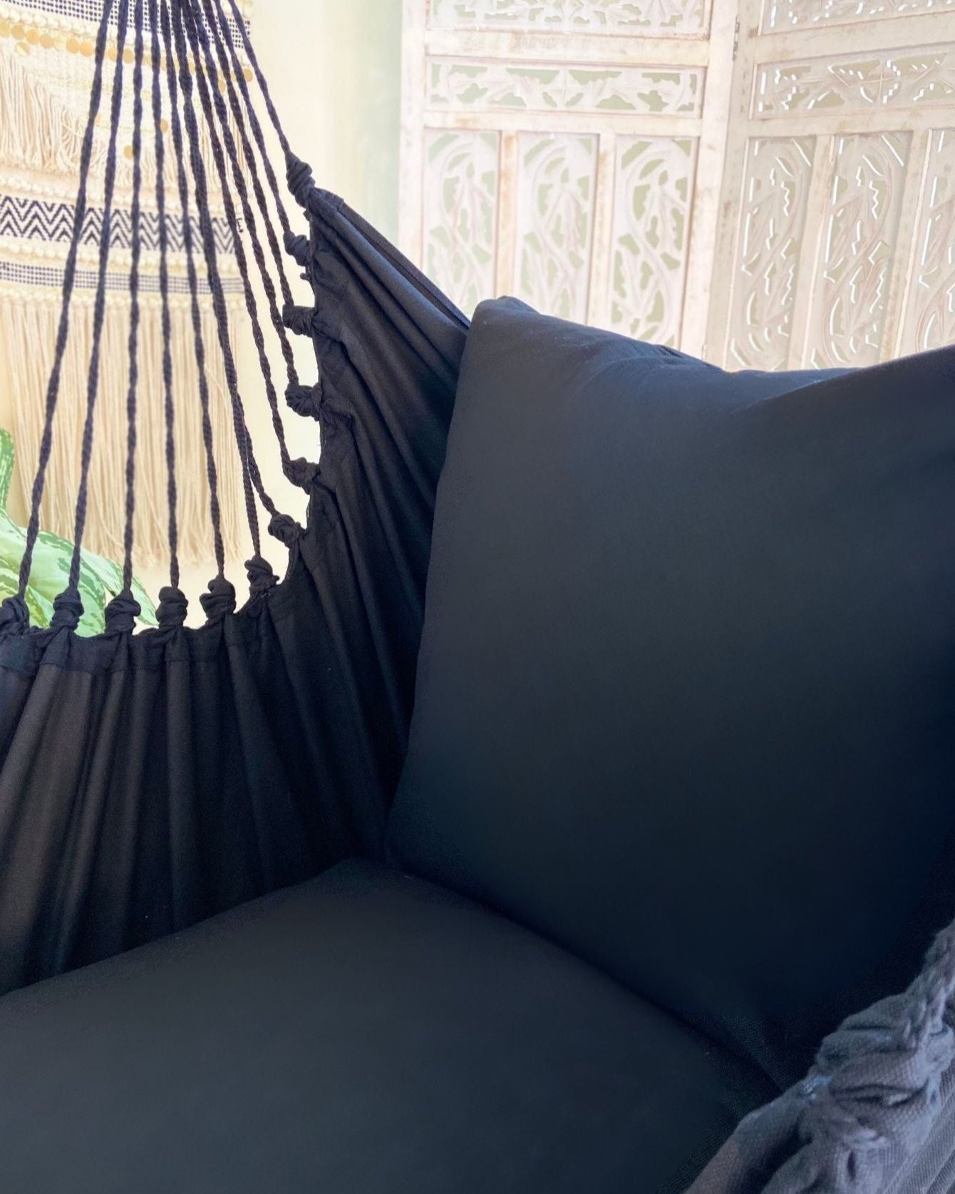 Black hammock with a pillow against a decorative wall.